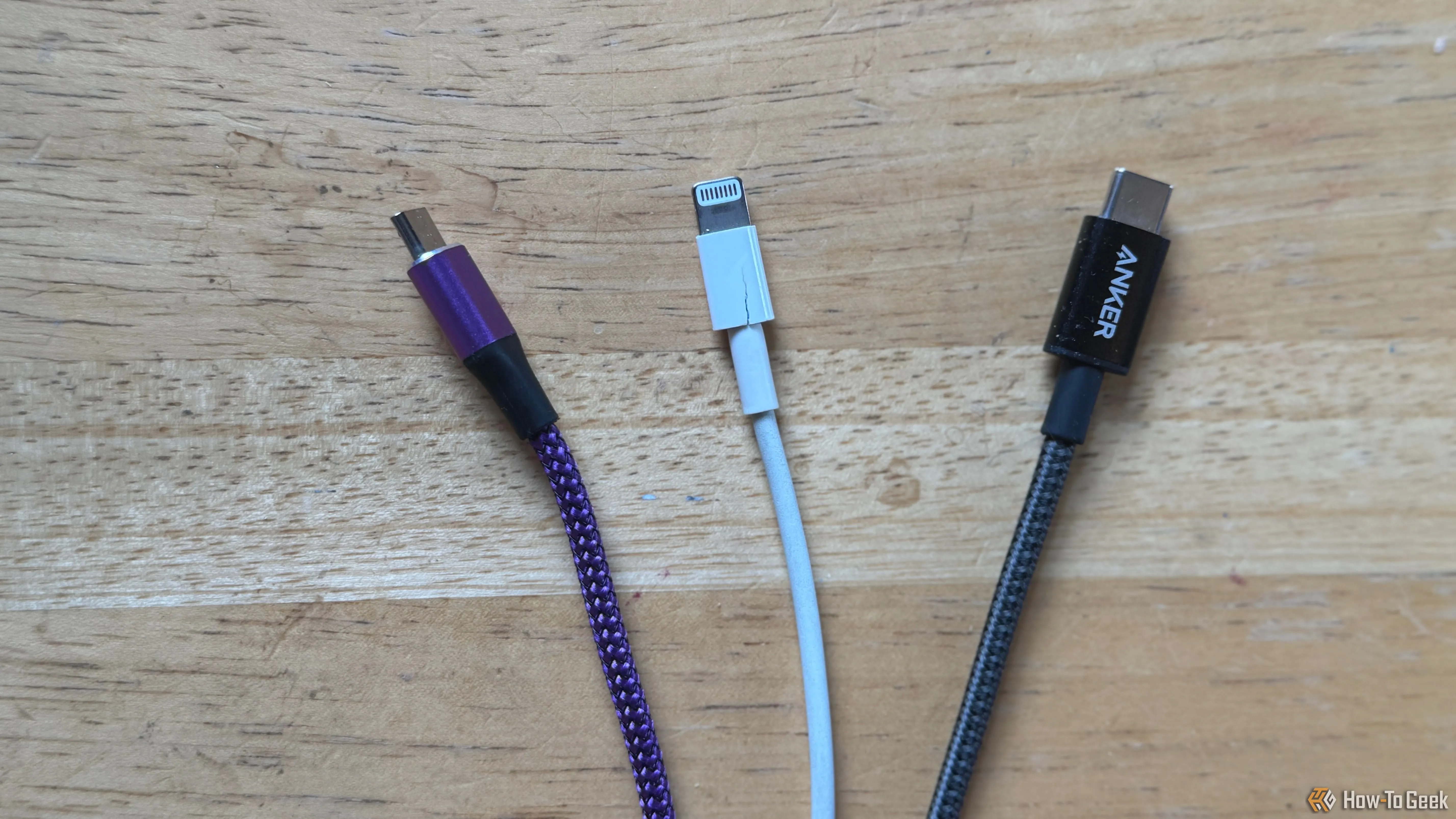 Bàn làm việc với cáp Micro-USB màu tím, cáp Lightning màu trắng và cáp USB-C màu xám, minh họa mẹo phân loại cáp sạc theo màu sắc.