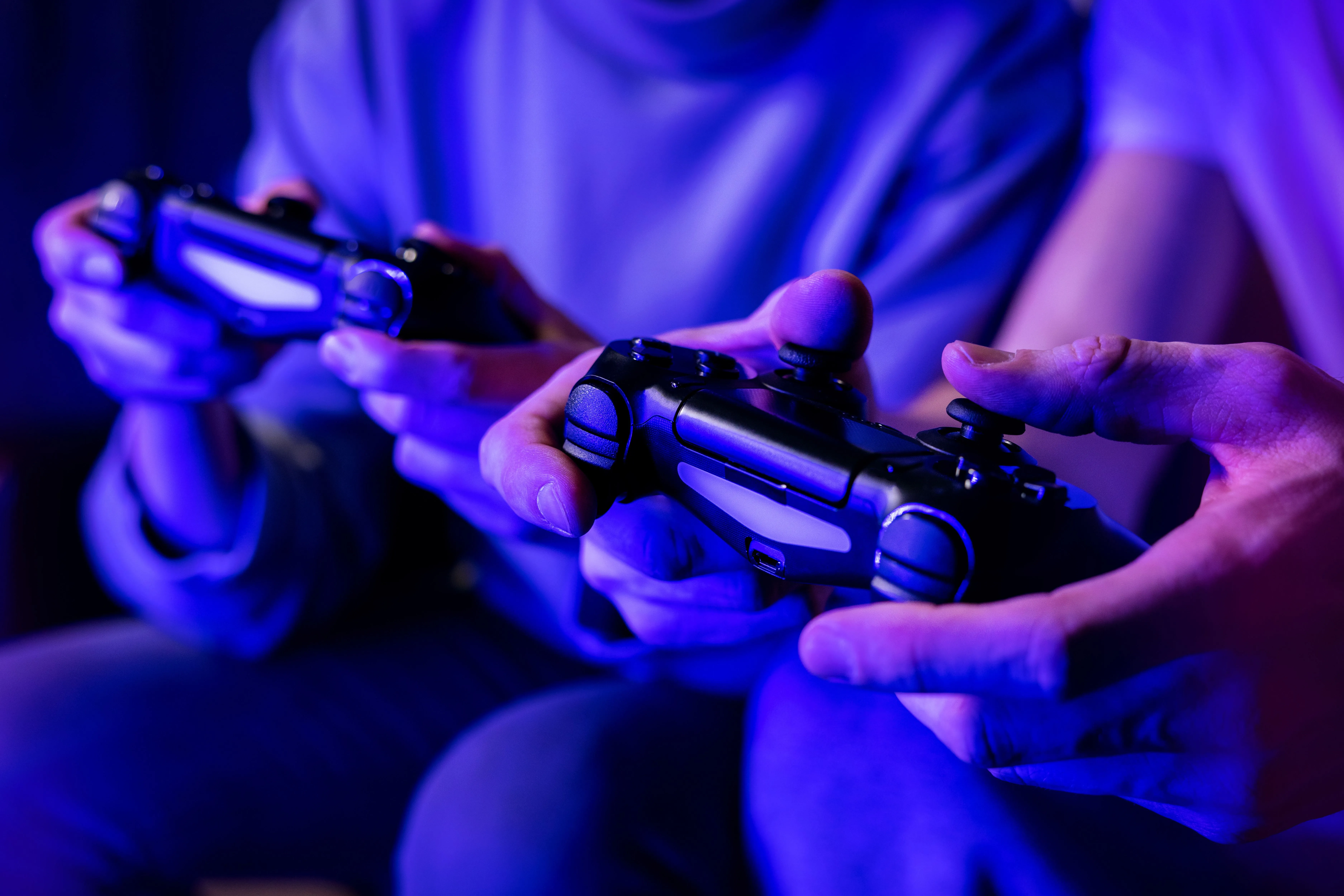 Hai người bạn đang chơi game cùng nhau trên ghế sofa, tượng trưng cho niềm vui và sự kết nối khi chơi game đa người.