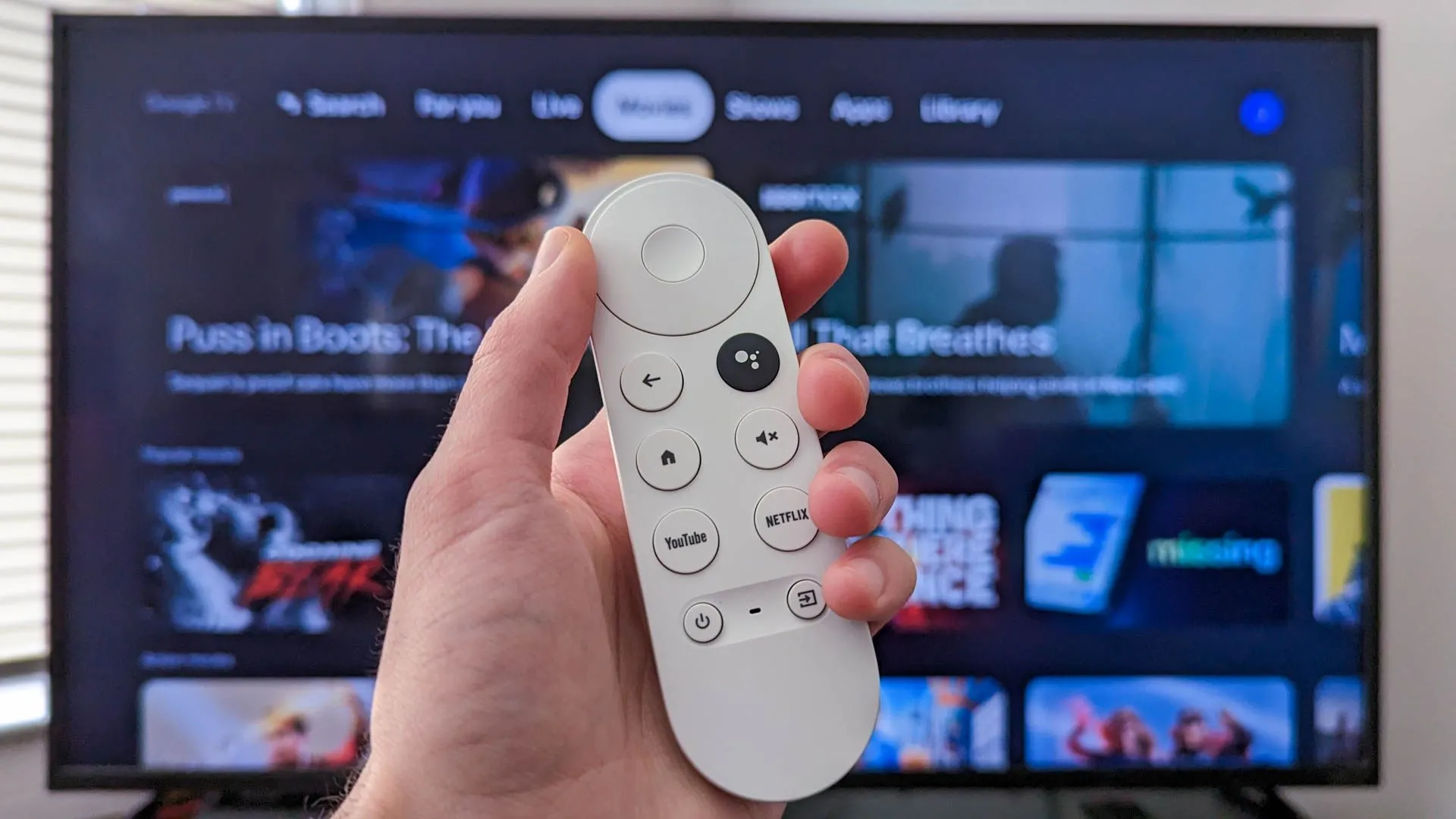 Thiết bị Chromecast with Google TV đang cắm vào TV, hiển thị giao diện Google TV