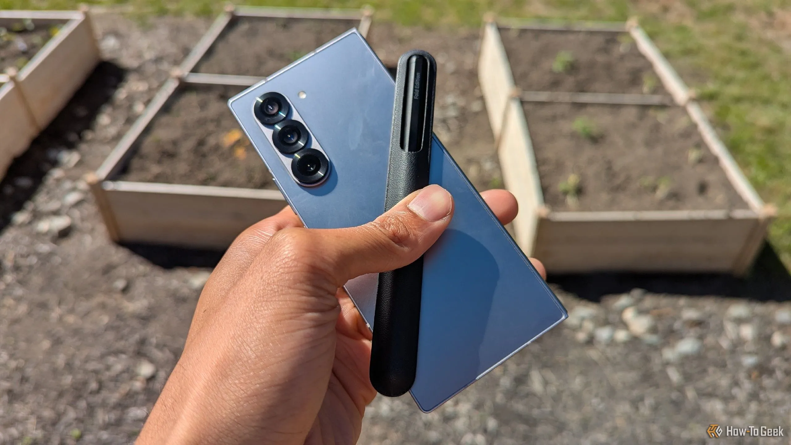 Điện thoại Samsung Galaxy Z Fold 6 và bút S Pen đặt trước khu vườn, thể hiện thiết bị nguyên bản sau nhiều lần rơi.
