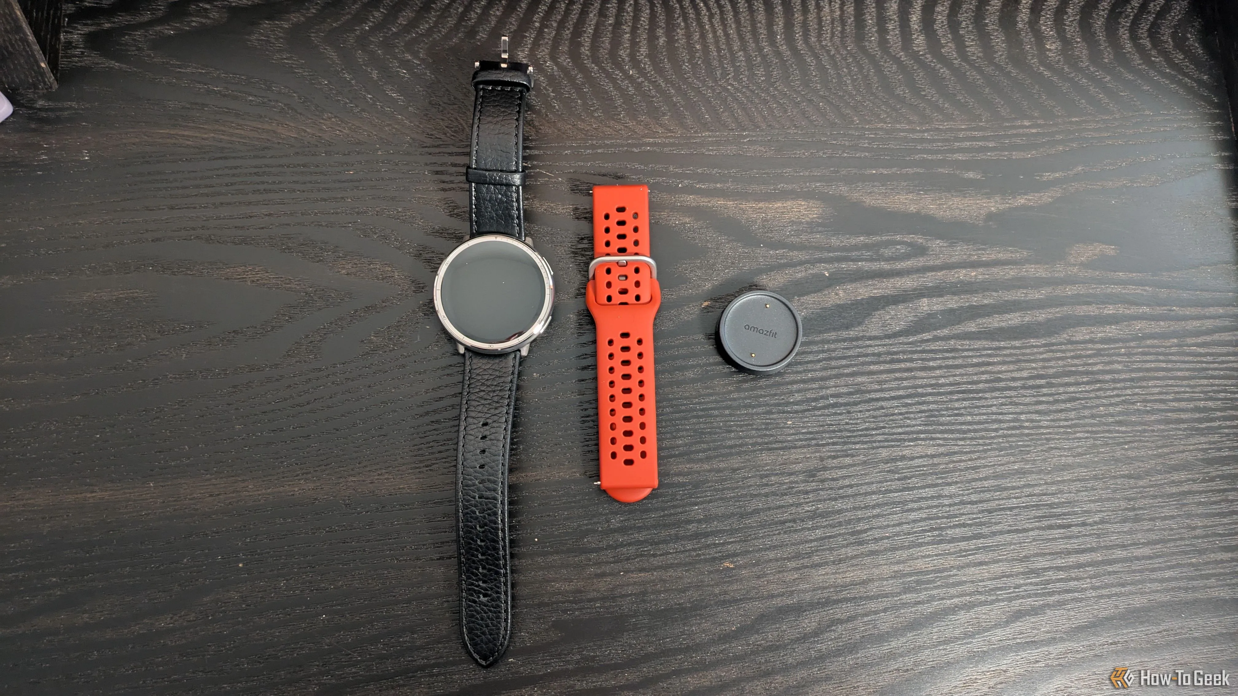 Đồng hồ Amazfit Active 2 màu đen, dây đeo phụ và đế sạc từ tính đặt trên mặt bàn.
