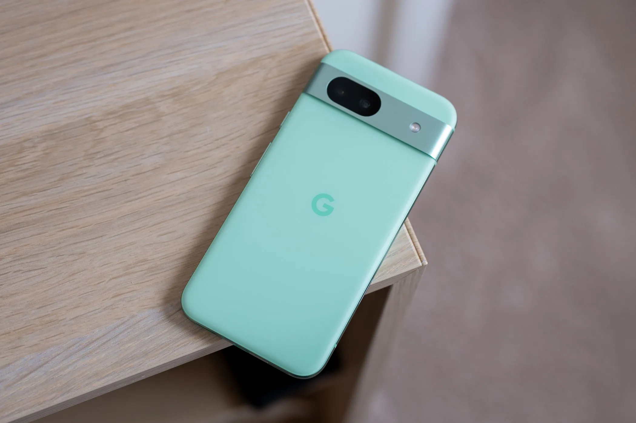Google Pixel 8a với thiết kế viền bo cong và cụm camera visor đặc trưng, đặt trên cạnh bàn.