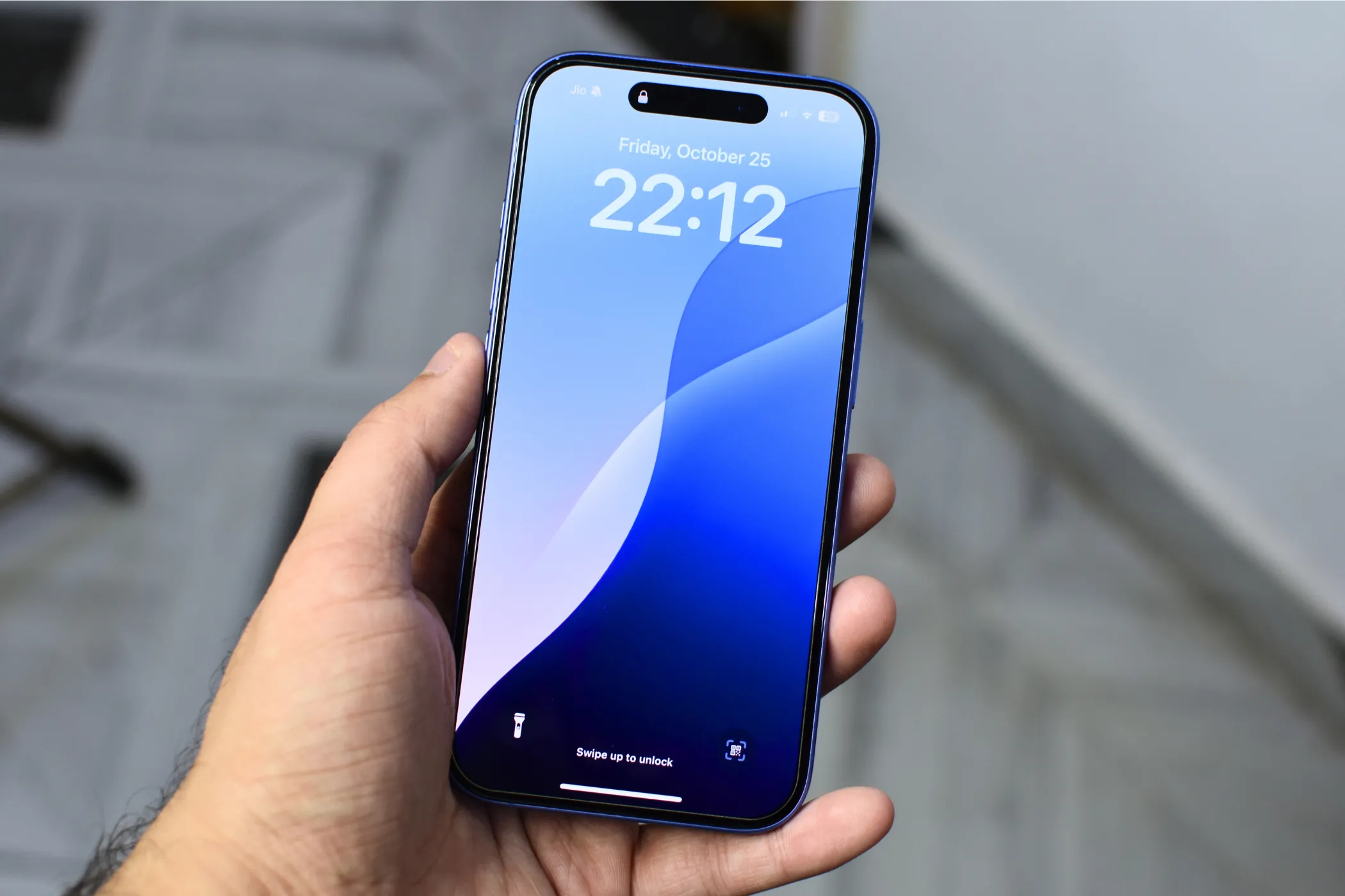 iPhone 16 màu xanh lam đang được cầm trên tay, màn hình hiển thị hình nền khóa màu xanh, minh họa dung lượng lưu trữ 128GB cơ bản và vấn đề không gian lưu trữ trên các dòng iPhone mới.