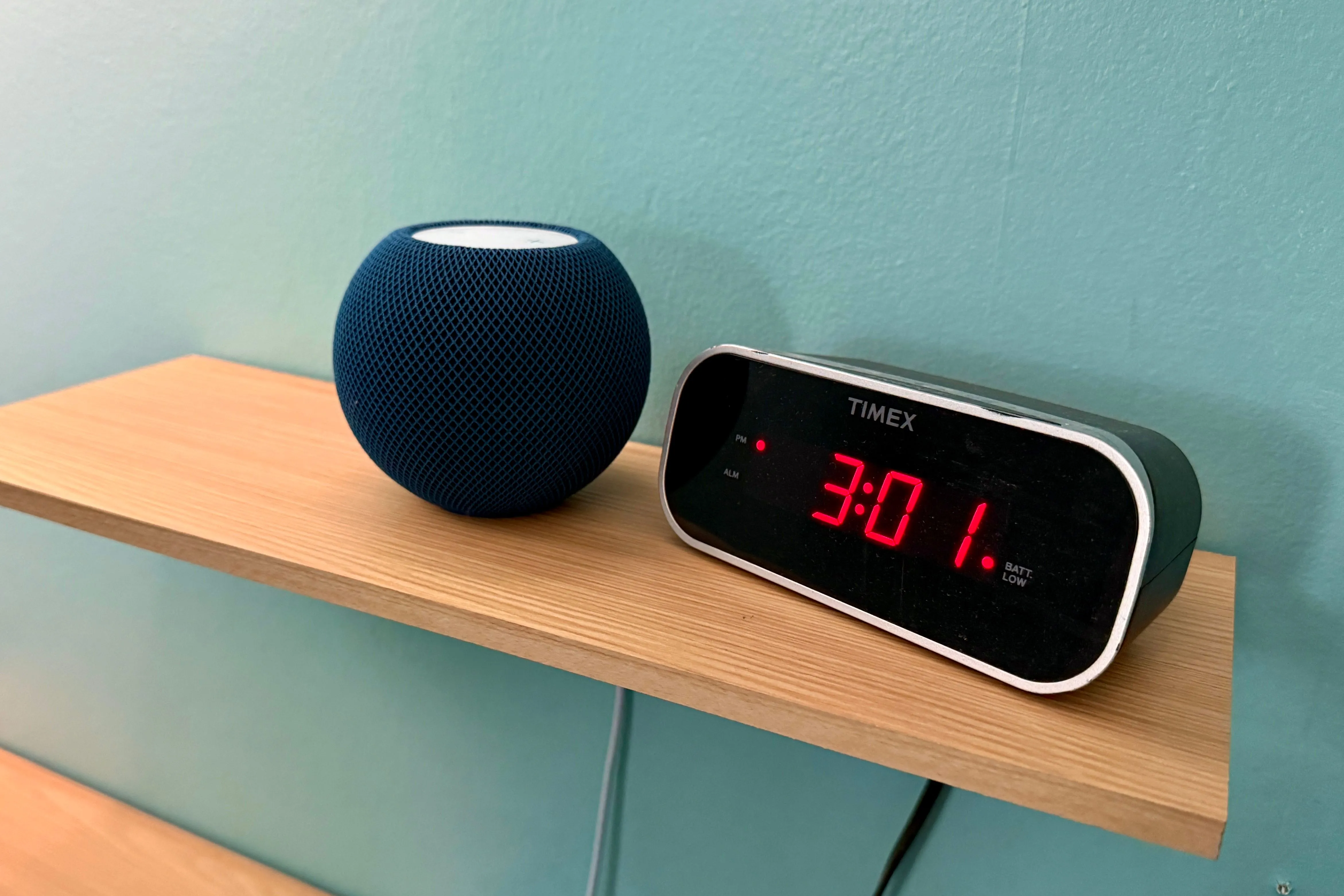 Loa thông minh Apple HomePod mini màu trắng đặt cạnh đồng hồ kỹ thuật số, thể hiện sự nhỏ gọn và khả năng hòa nhập vào không gian sống hiện đại