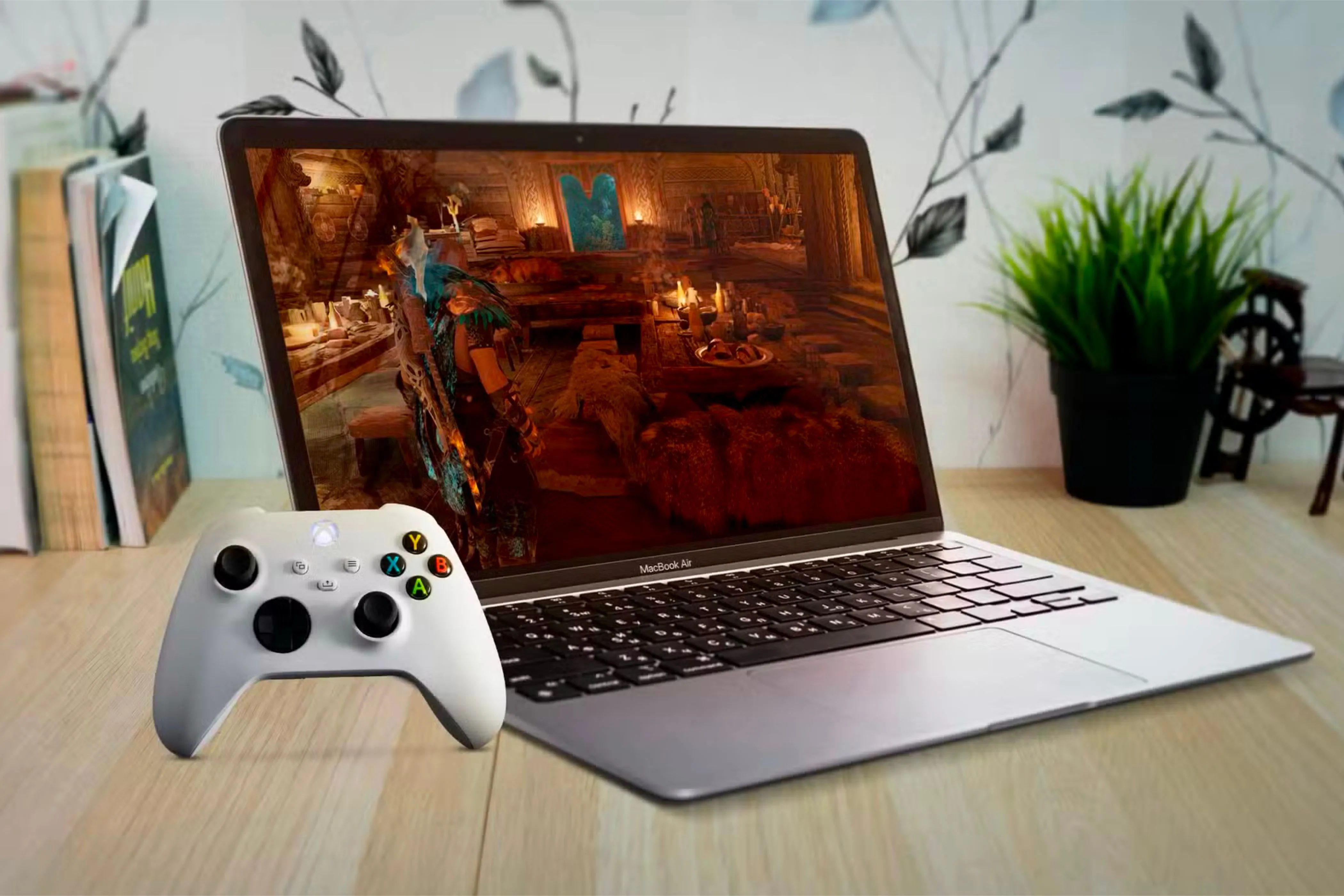 Một chiếc MacBook Air đặt dưới bàn gỗ, màn hình hiển thị trò chơi và tay cầm Xbox bên cạnh, thể hiện khả năng giải trí trên Mac