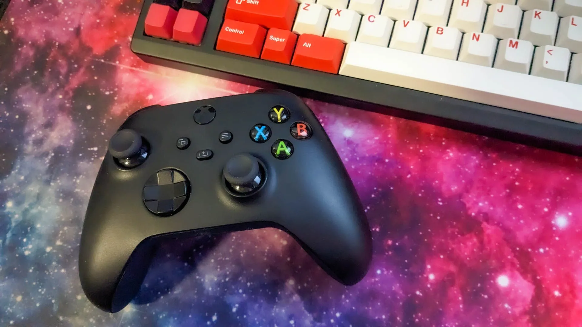 Tay cầm Xbox được đặt cạnh bàn phím cơ trên tấm lót chuột không gian.