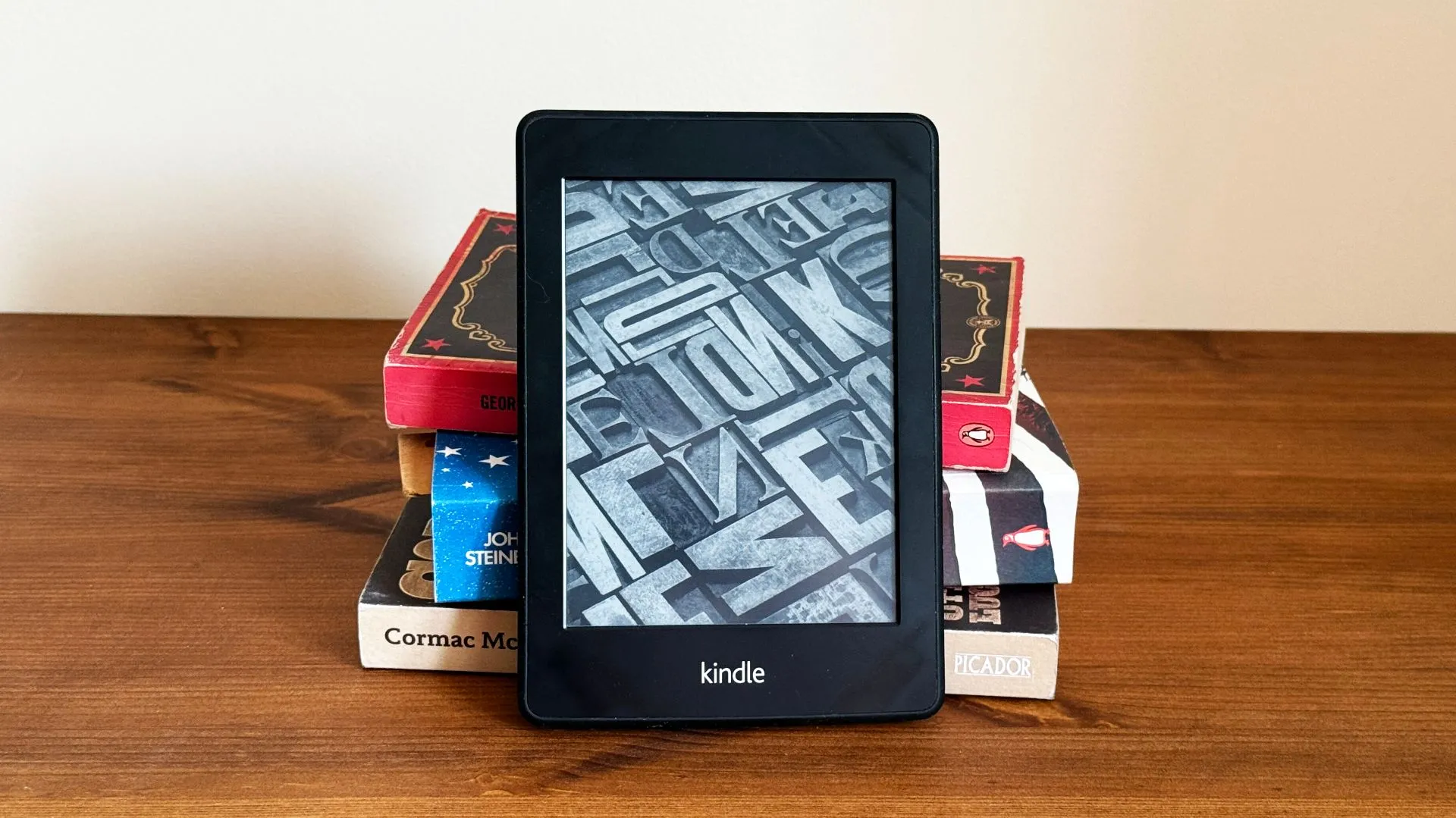Thiết bị đọc sách Kindle phía trước chồng sách giấy, minh họa tính năng lọc quảng cáo mới