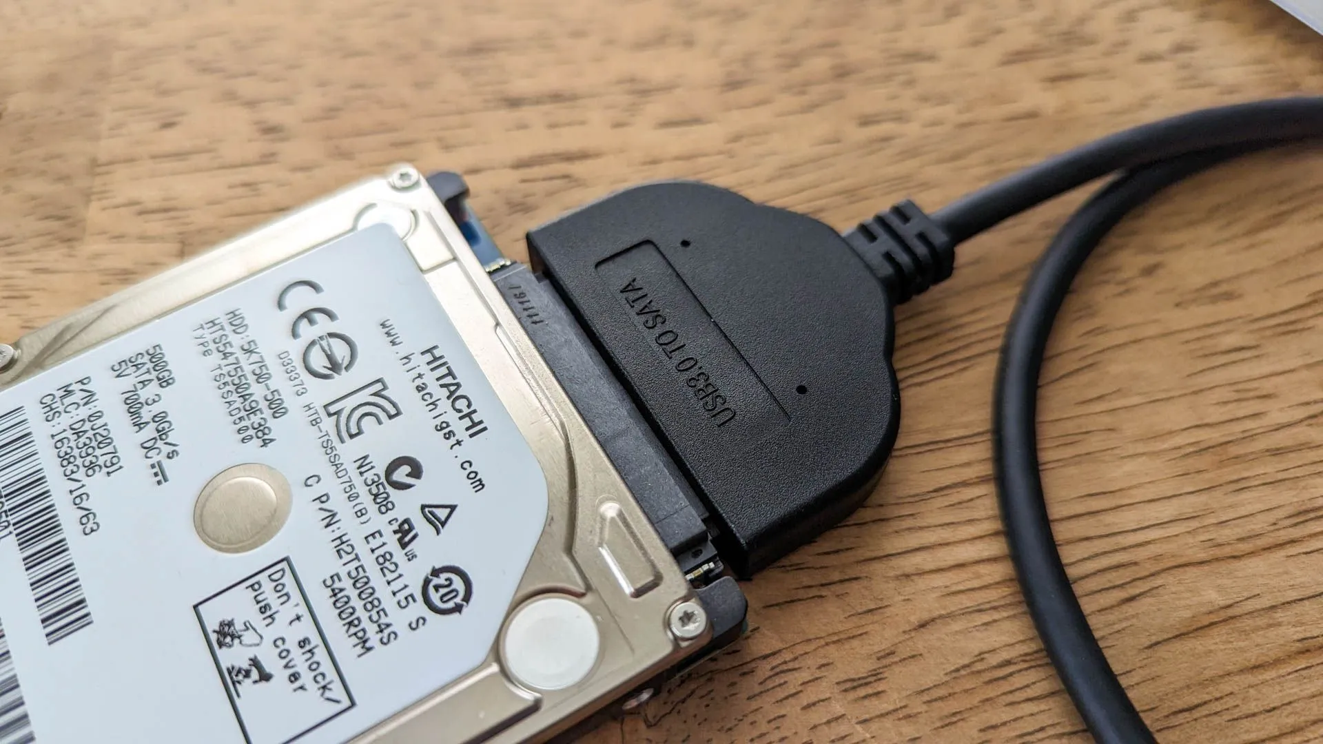Ổ cứng ngoài kết nối qua bộ chuyển đổi USB trên bề mặt gỗ.